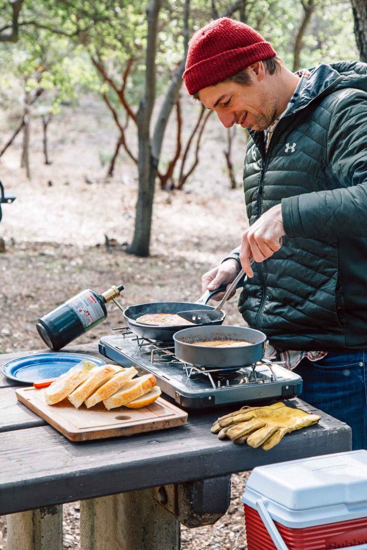 Michael cooking French toast on a camp stove with trees in the background