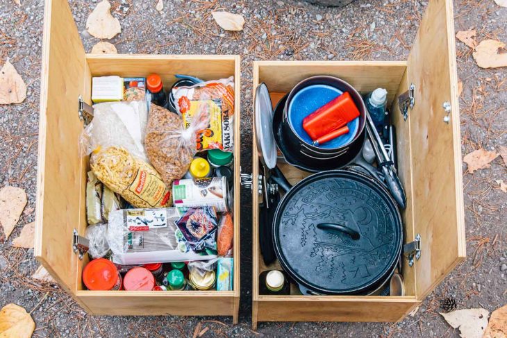 Two wooden crates filled with camping pantry ingredients and camp cooking equipment
