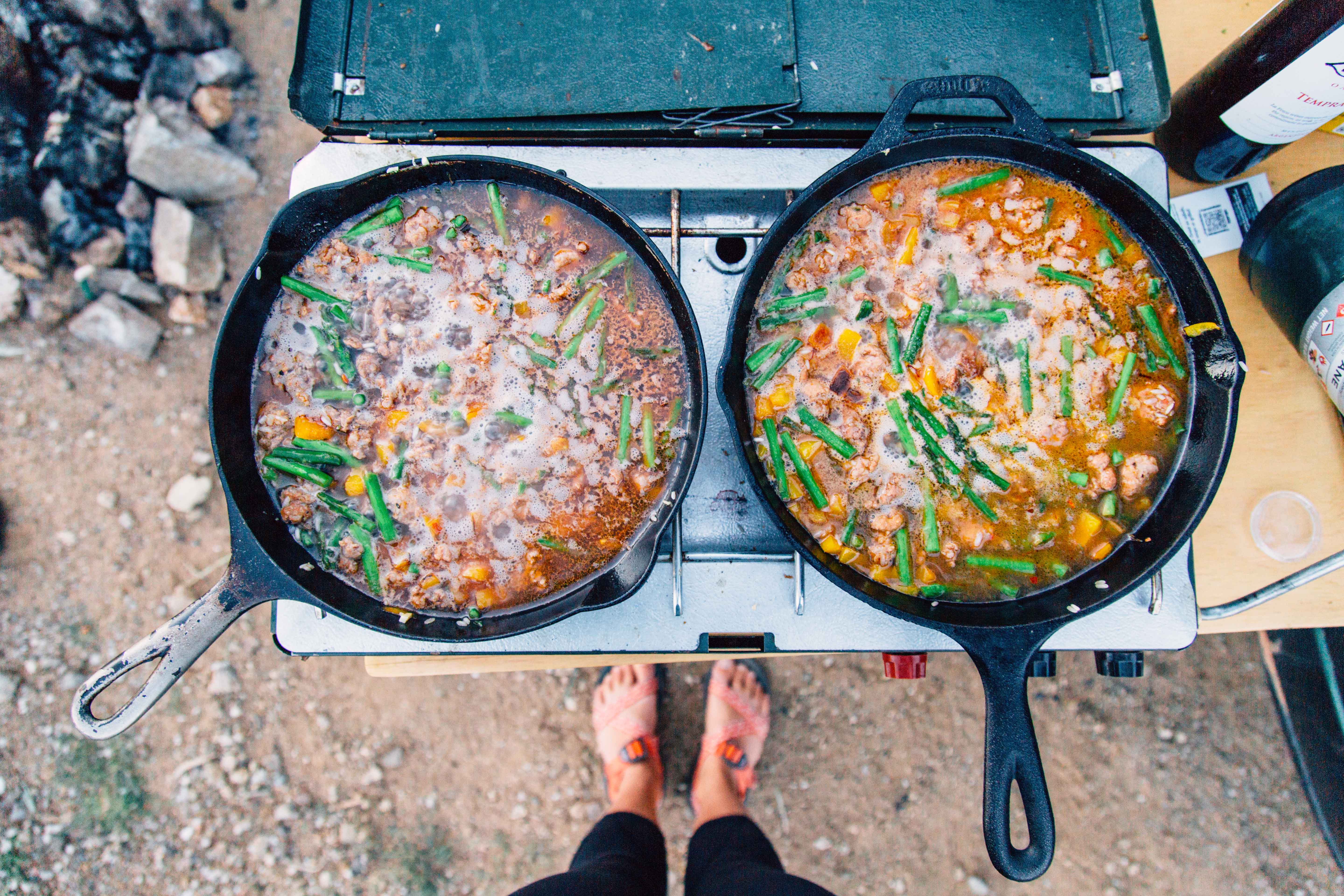 Two cast iron skillets full of food on a camp stove