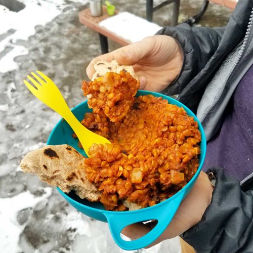 Woman holding a bowl of dhal and a piece of roti