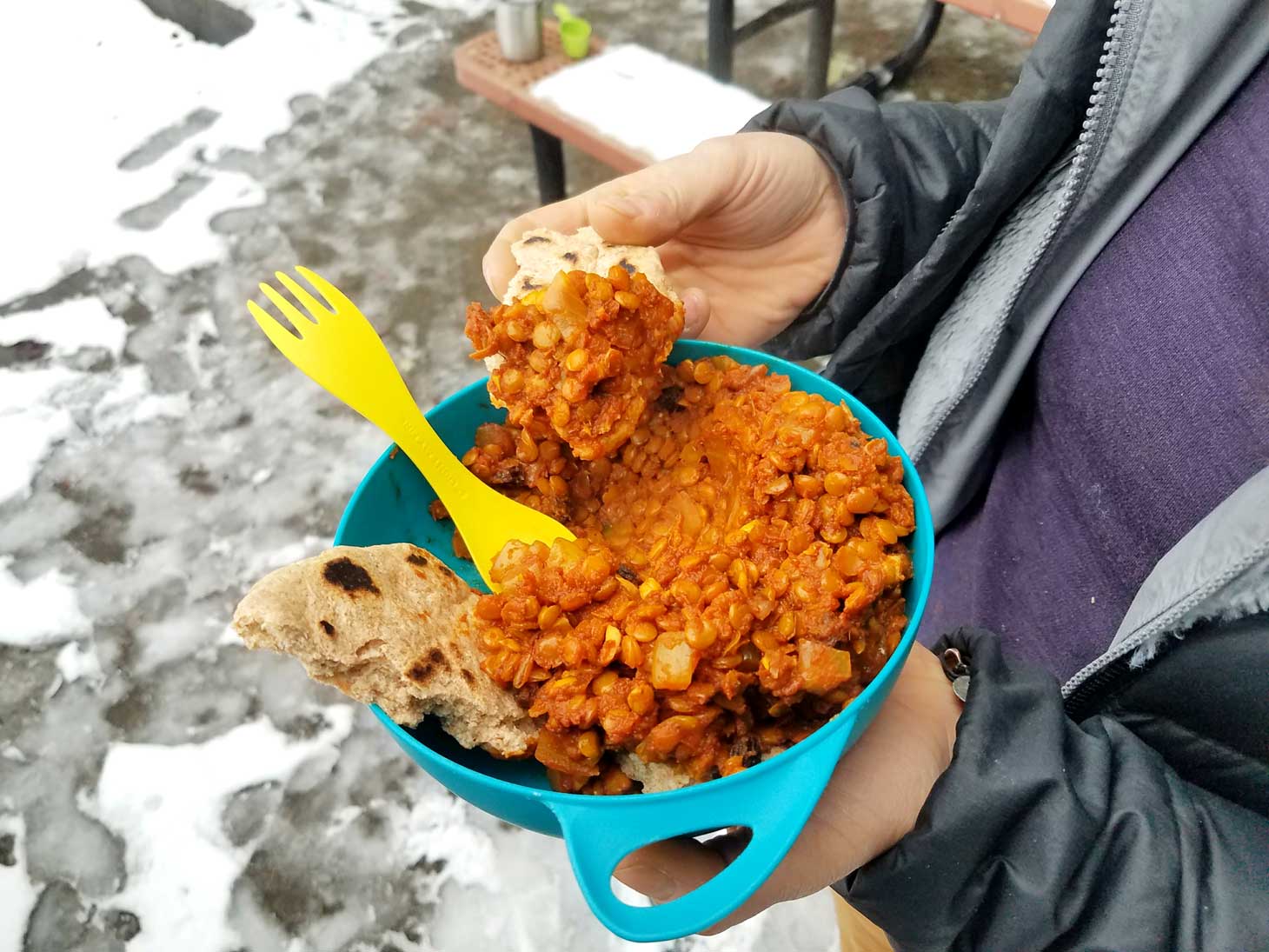 Woman holding a bowl of dhal and a piece of roti