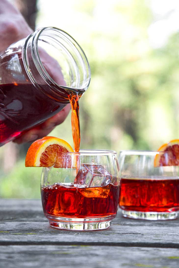 Pouring Negroni cocktail mix from a mason jar into a cocktail glass