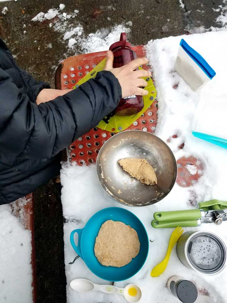 Rolling roti dough on a small cutting board on a snowy table