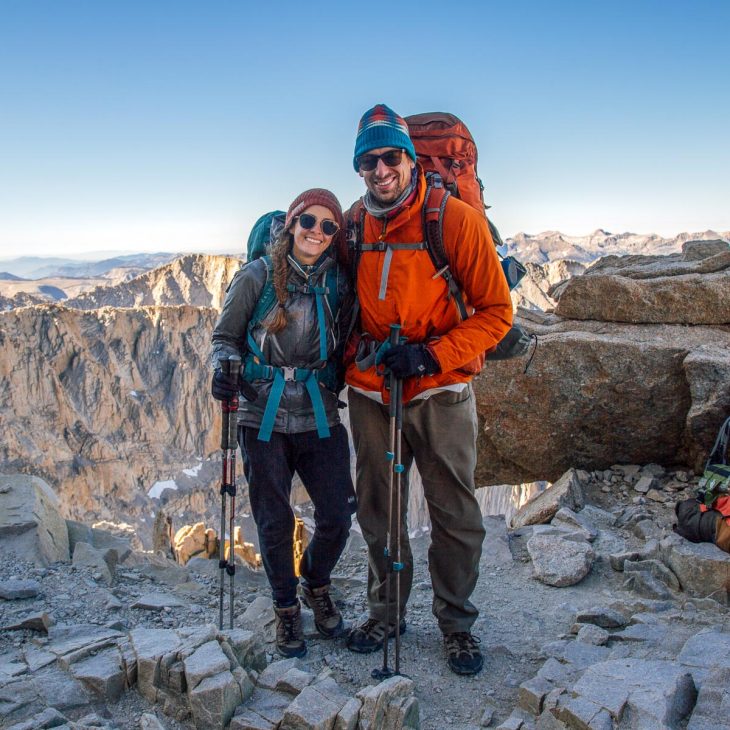 Megan and Michael wearing their backpacking packs. They are smiling and there are mountain peaks in the distance