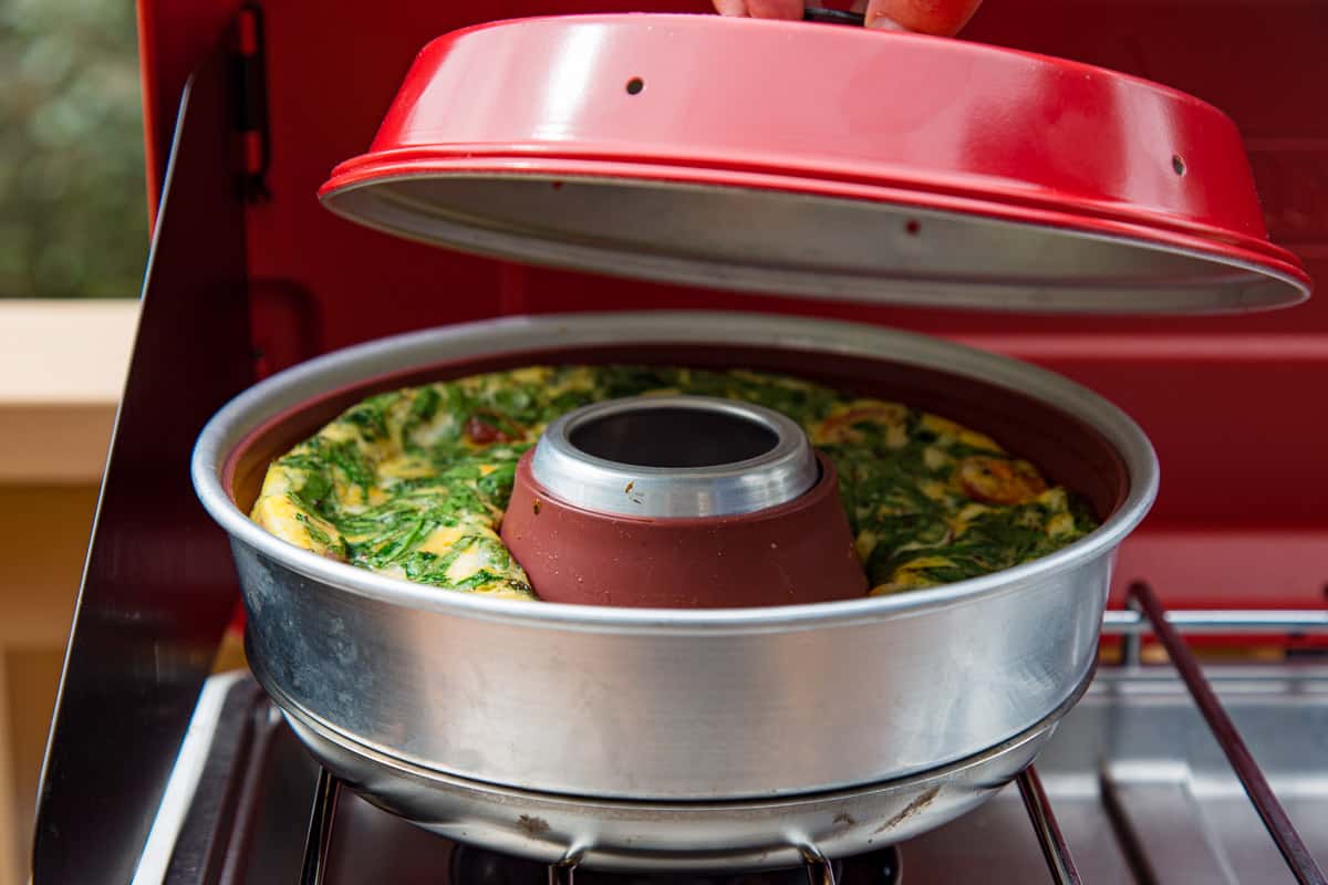 Michael lifting the lid off of an omnia oven that is sitting on a camp stove