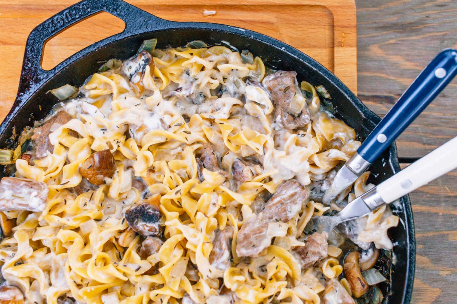 Beef stroganoff in a cast iron skillet on a wooden cutting board