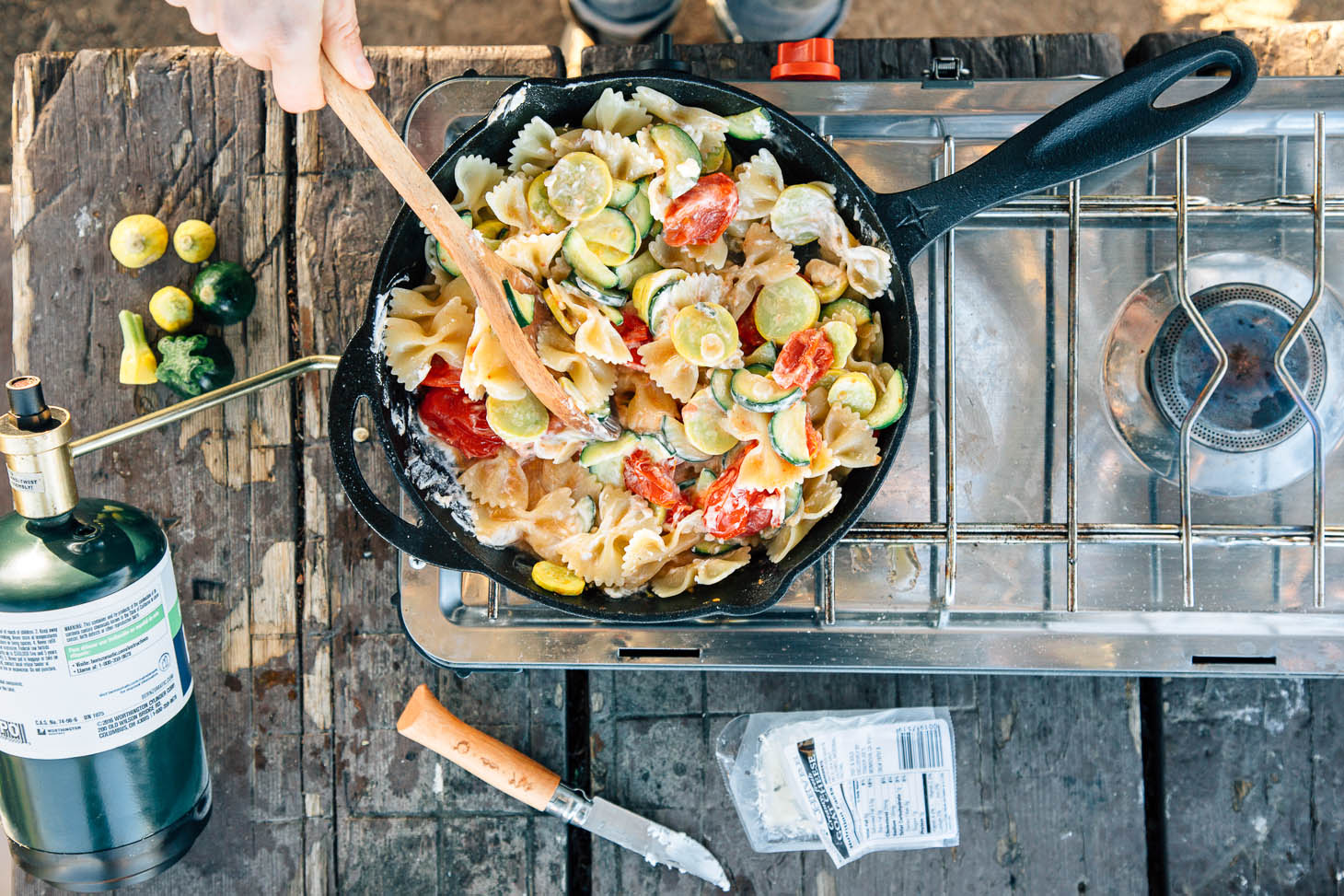 Squash, zucchini, tomatoes, and pasta in a cast iron skillet on a camping stove.