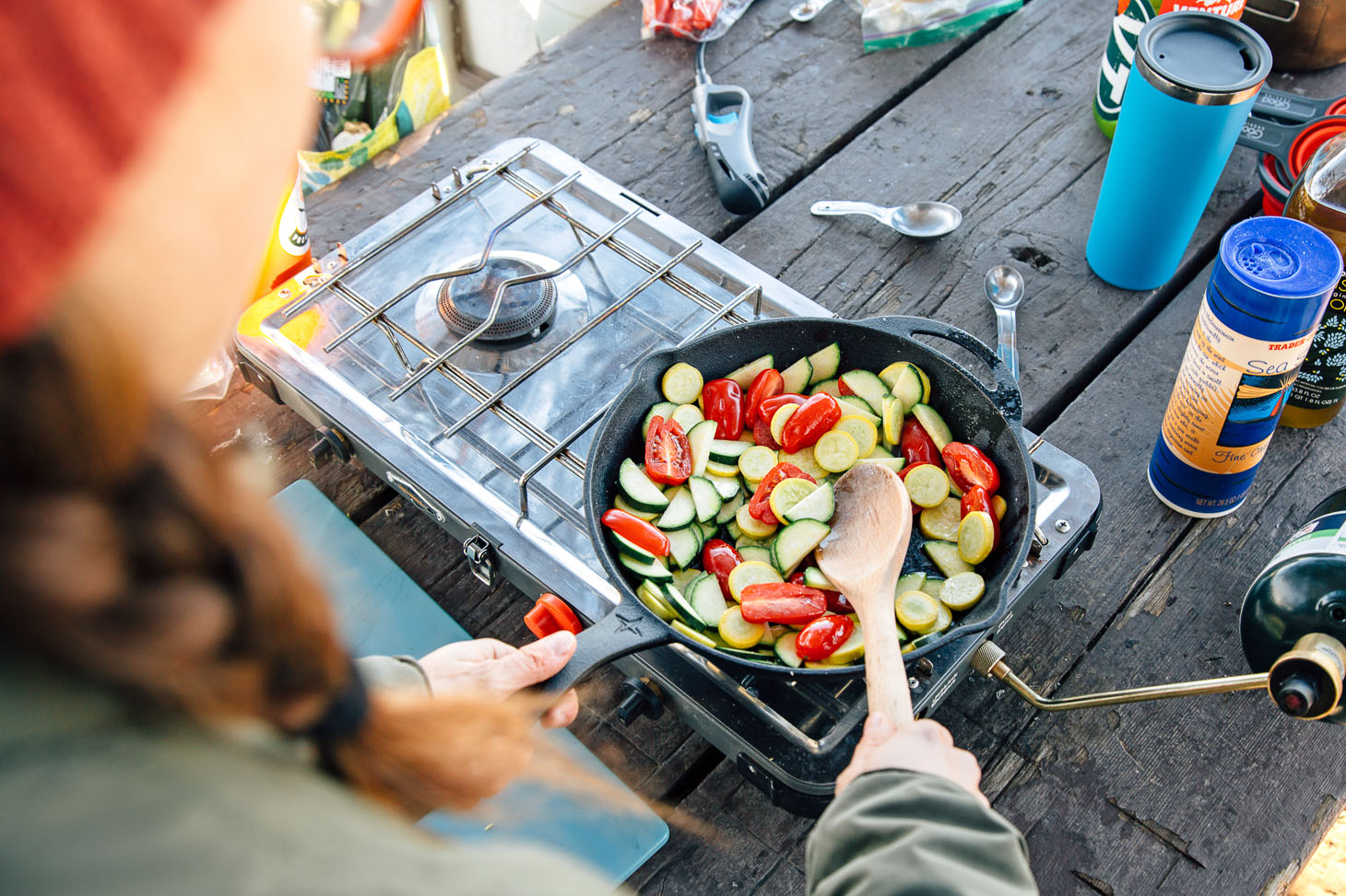 Sauteeing tomatoes, zucchini, and yellow summer squash in a cast iron skillet on a camping stove.