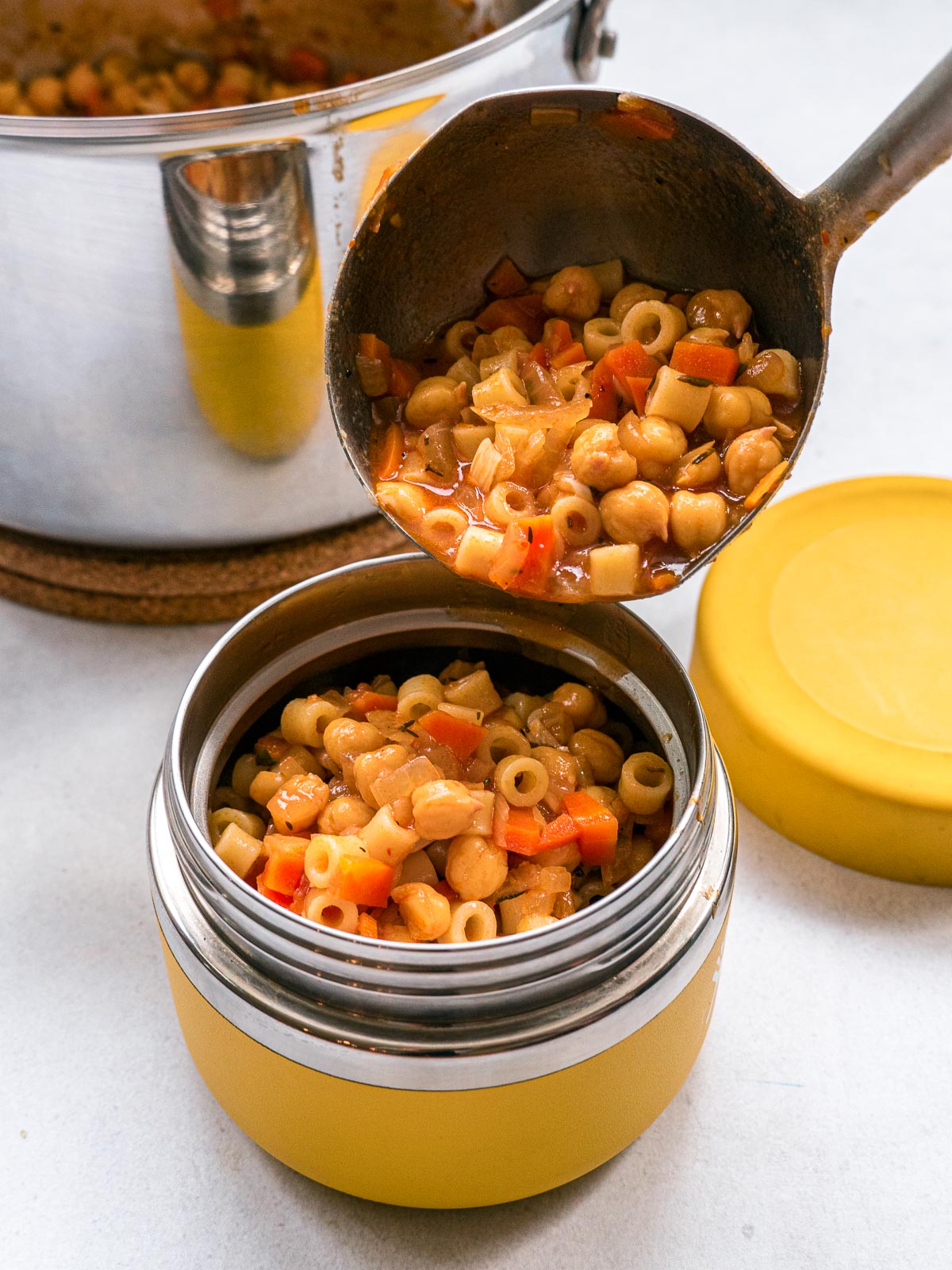 Ladling pasta e ceci into a yellow insulated container