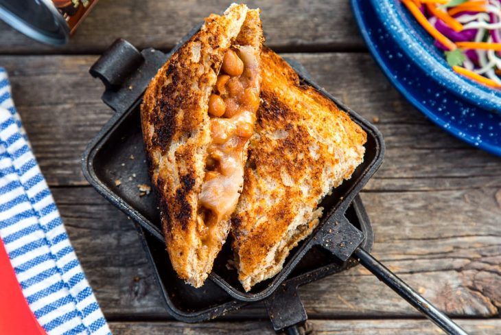 A sandwich filled with beans and cheese cut diagonally in half, resting on a open pie iron