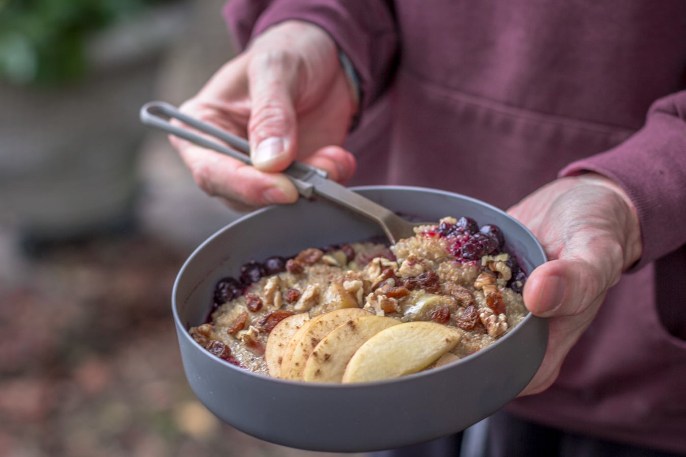 Holding a bowl of breakfast quinoa porridge with apples.