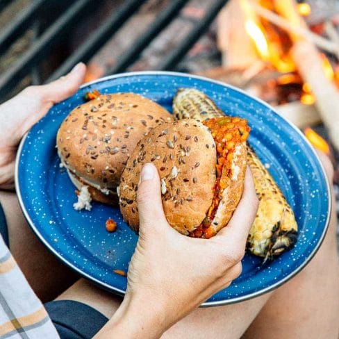 Megan holding a plate with two sloppy joes and an ear of grilled corn. She is picking up one of the sandwiches.