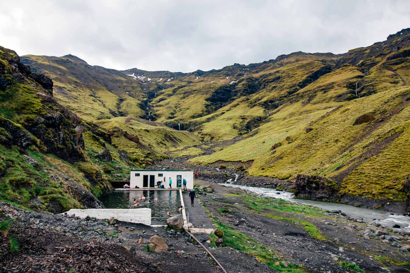 People swimming in the Seljavellir hot spring surrounded by green hills