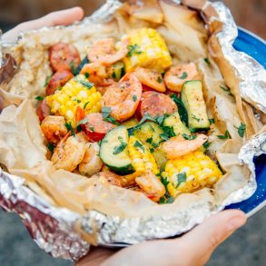 Woman holding a shrimp boil foil packet on a blue plate