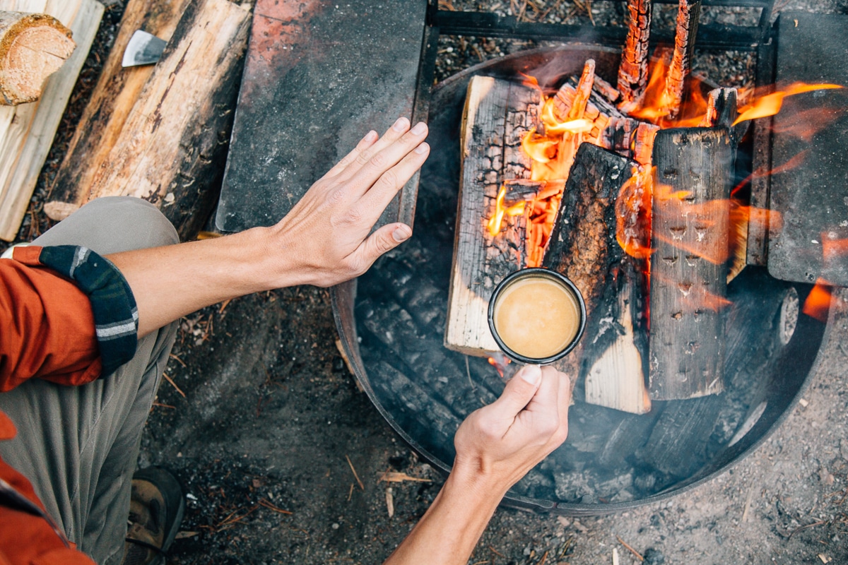 Michael holding a mug and warming his hands over a campfire