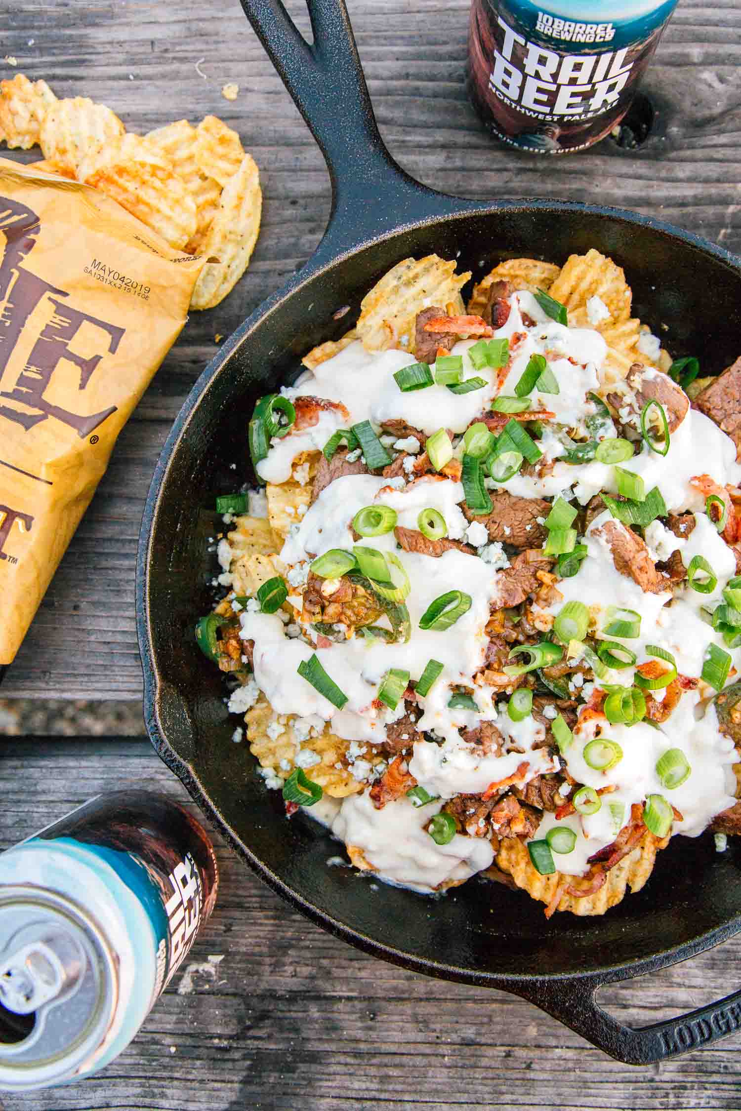 Overhead shot of cast iron skillet nachos. A bag of chips and a can of beer are in frame.