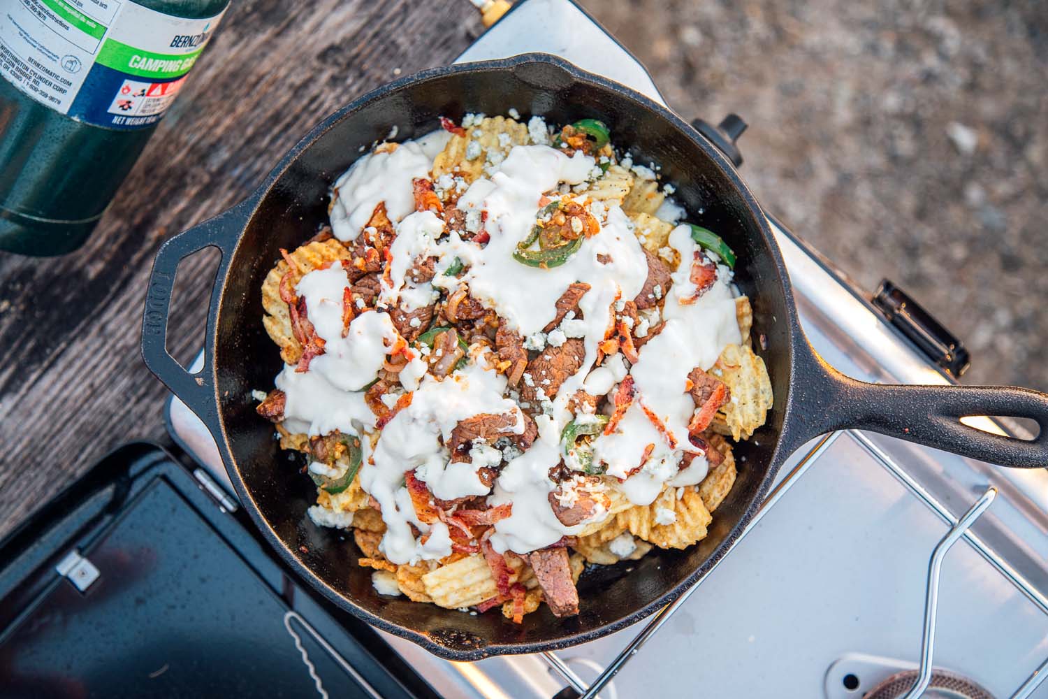 Overhead shot of nachos in a cast iron skillet on a camping stove.