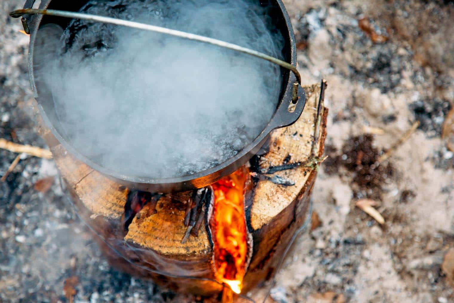 A Dutch oven with boiling water on top of a Swedish firelog