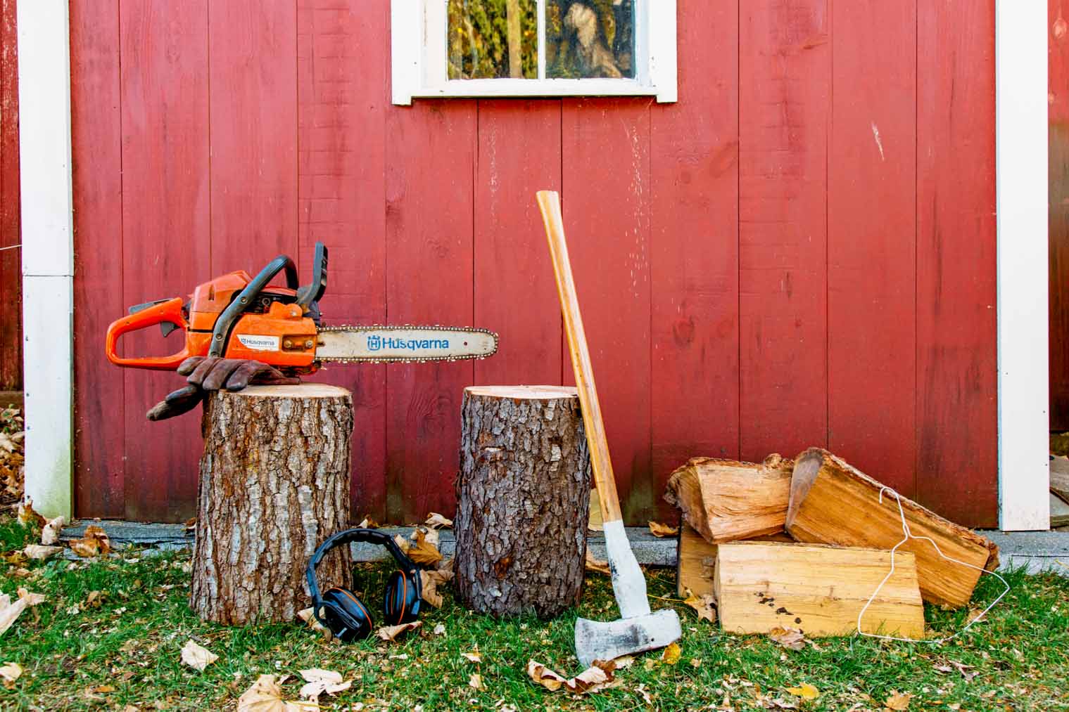 Firewood and wood cutting tools in front of a red shed