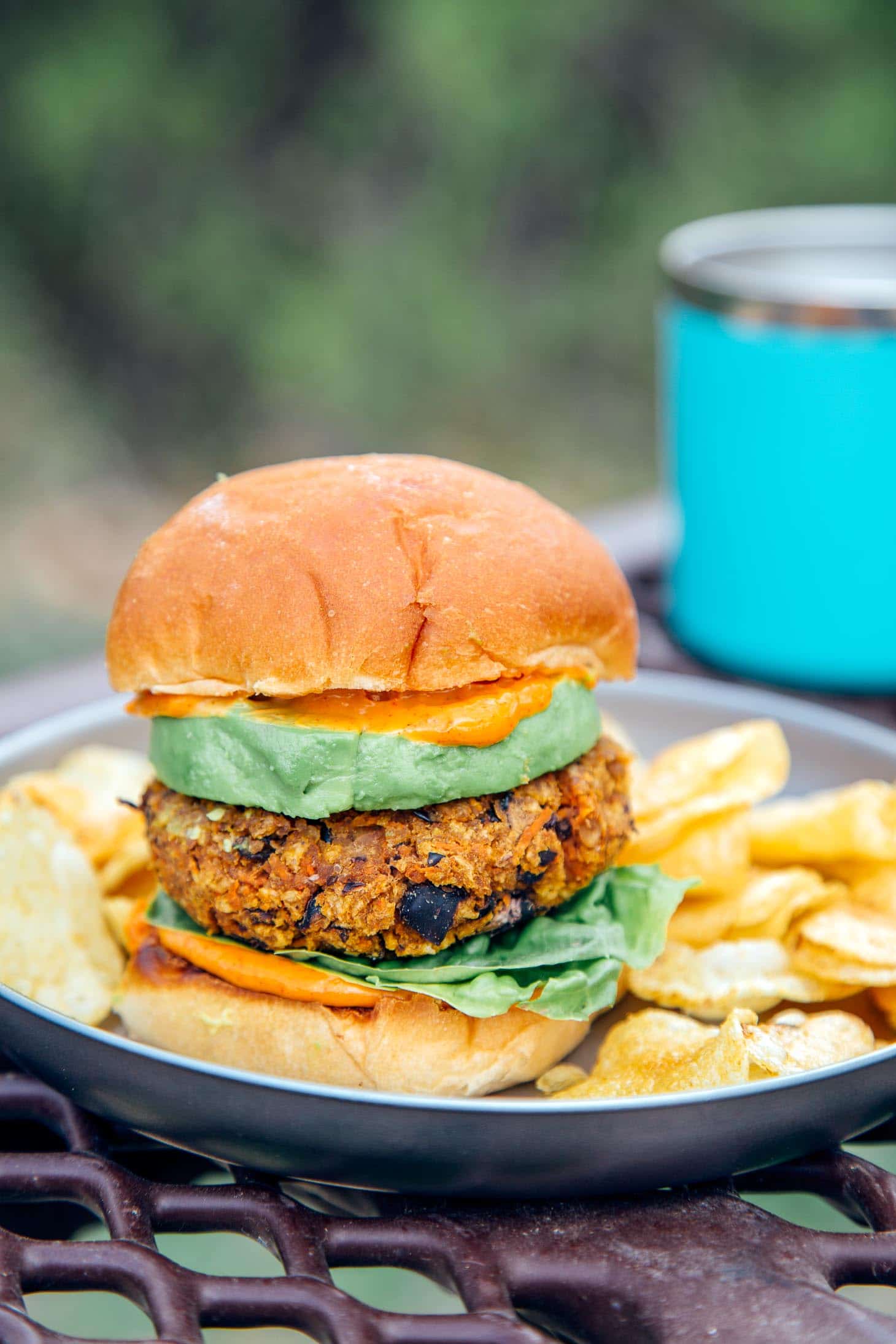 A sweet potato black bean burger stacked between two buns, avocado, and spicy mayo on a plate with a natural backdrop.