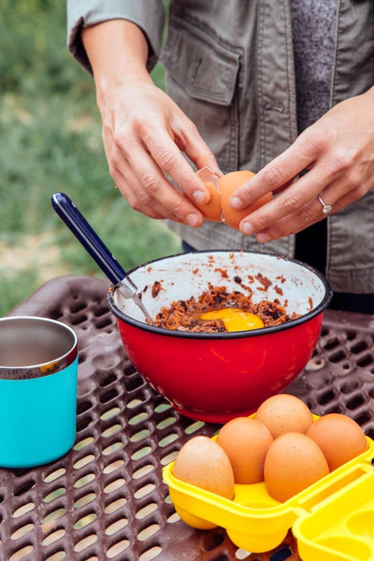 Cracking an egg into a red bowl with other black bean burger ingredients.