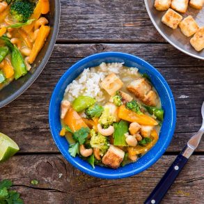 A blue bowl filled with Thai green curry on a wooden camping table