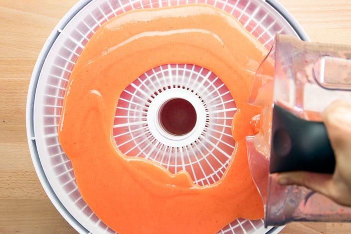 Pouring pureed fruit onto a dehydrator tray.