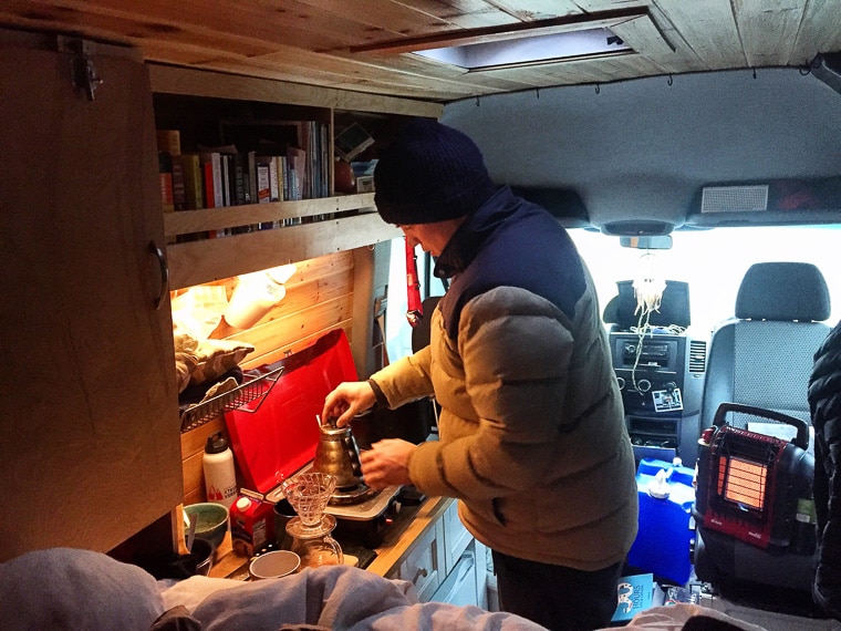 A man making coffee at a stove inside of a camper van