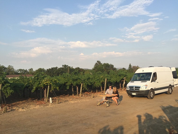 A man and a woman sitting at a table in front of their sprinter camper van