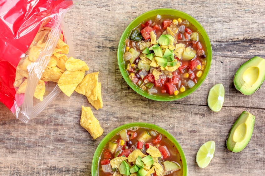 Tortilla soup in a bowl with slices of avocado and tortilla chips next on the side