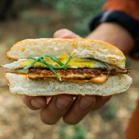 A person holding half an egg and halloumi cheese sandwich.