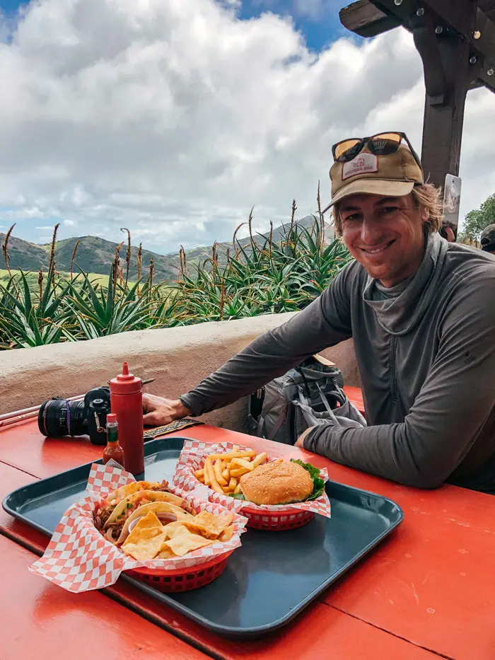 Man sitting at a red table with a tray of burgers and tacos