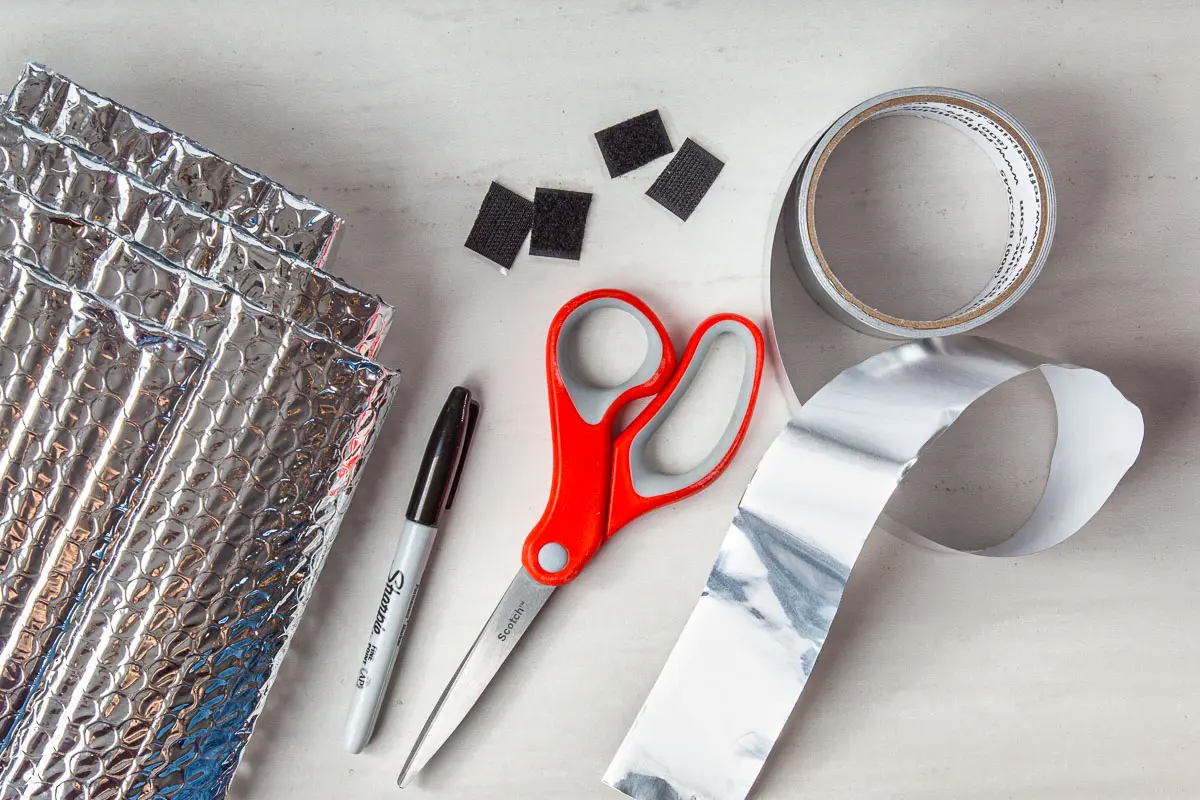 Materials for a pot cozy laid out: reflictix, foil tape, sharpie, scissors, velcro