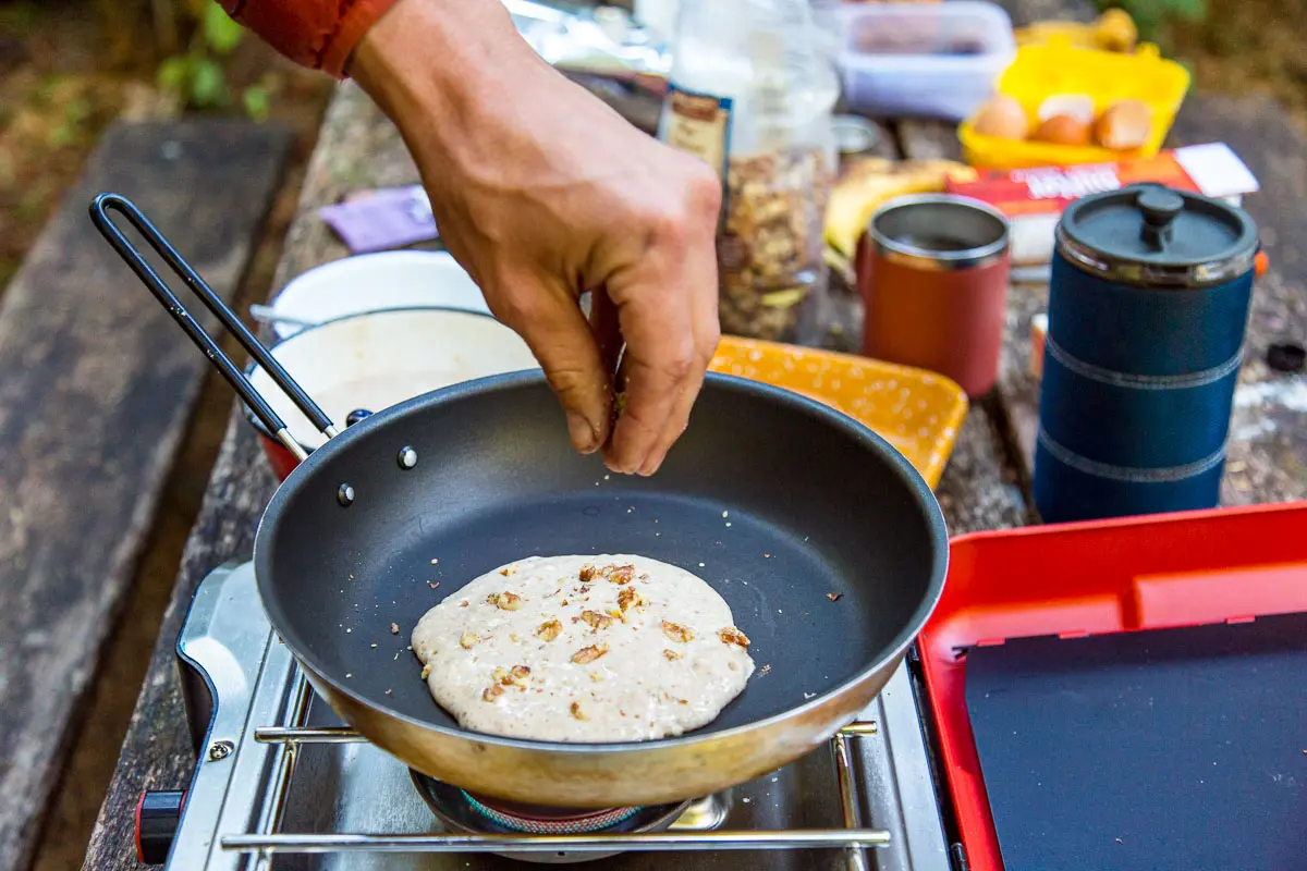 Michael sprinkling walnut into pancake batter on a skillet