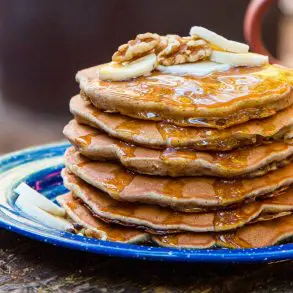 A stack of pancakes on a blue plate, topped with slices of bananas and walnuts.