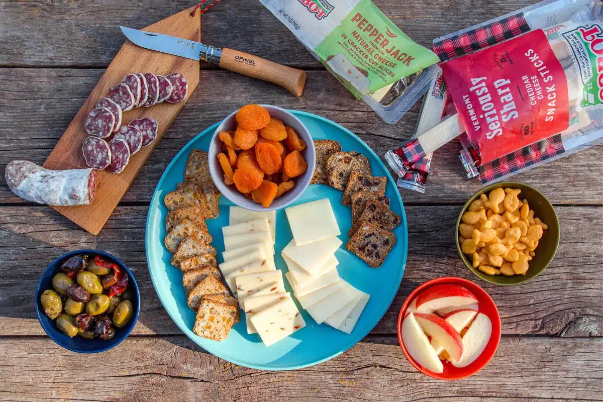 Cheese, fruit, salami, nuts, and crackers displayed on a camping table.