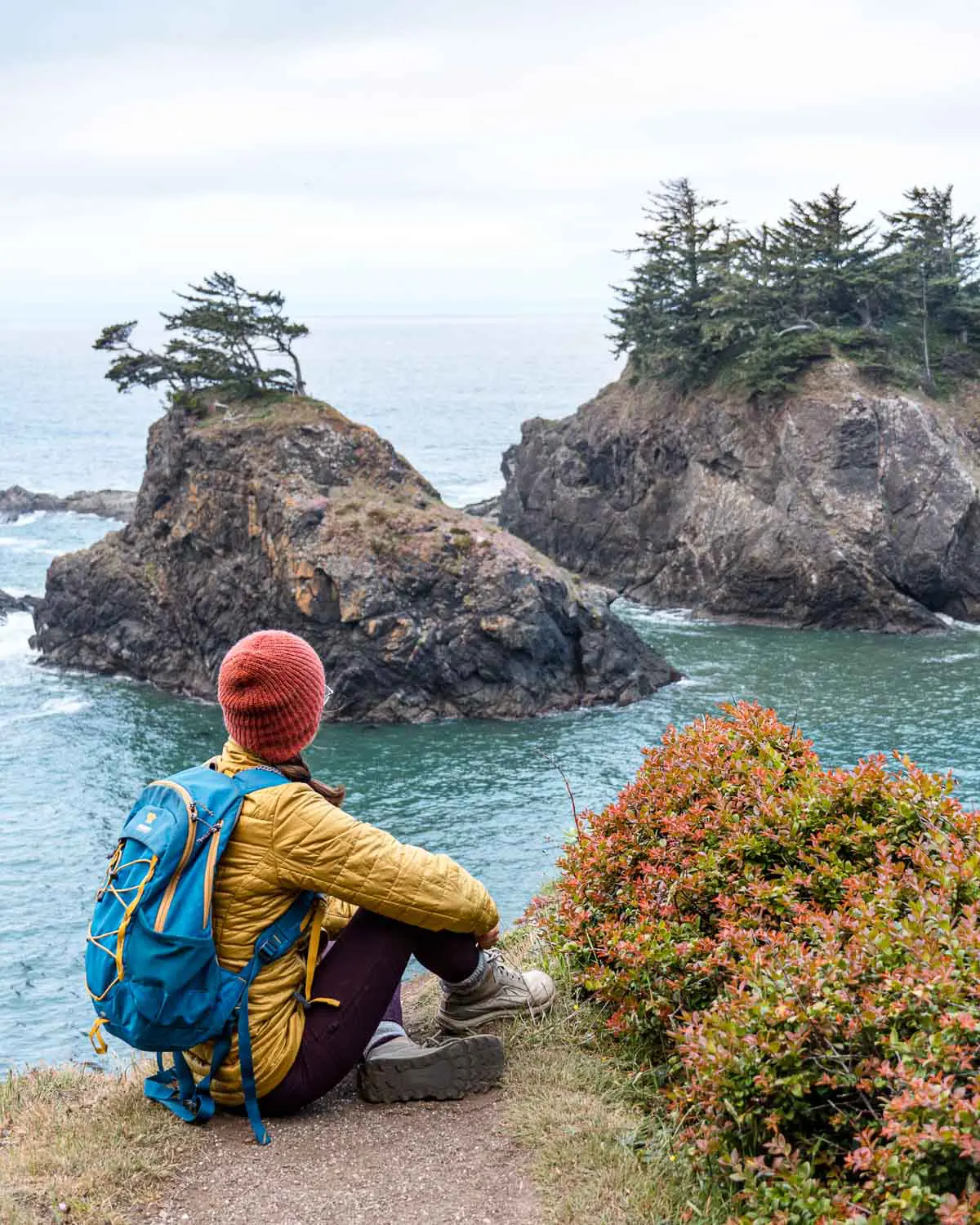 Megan is sitting on a cliff side looking out a sea stacks.