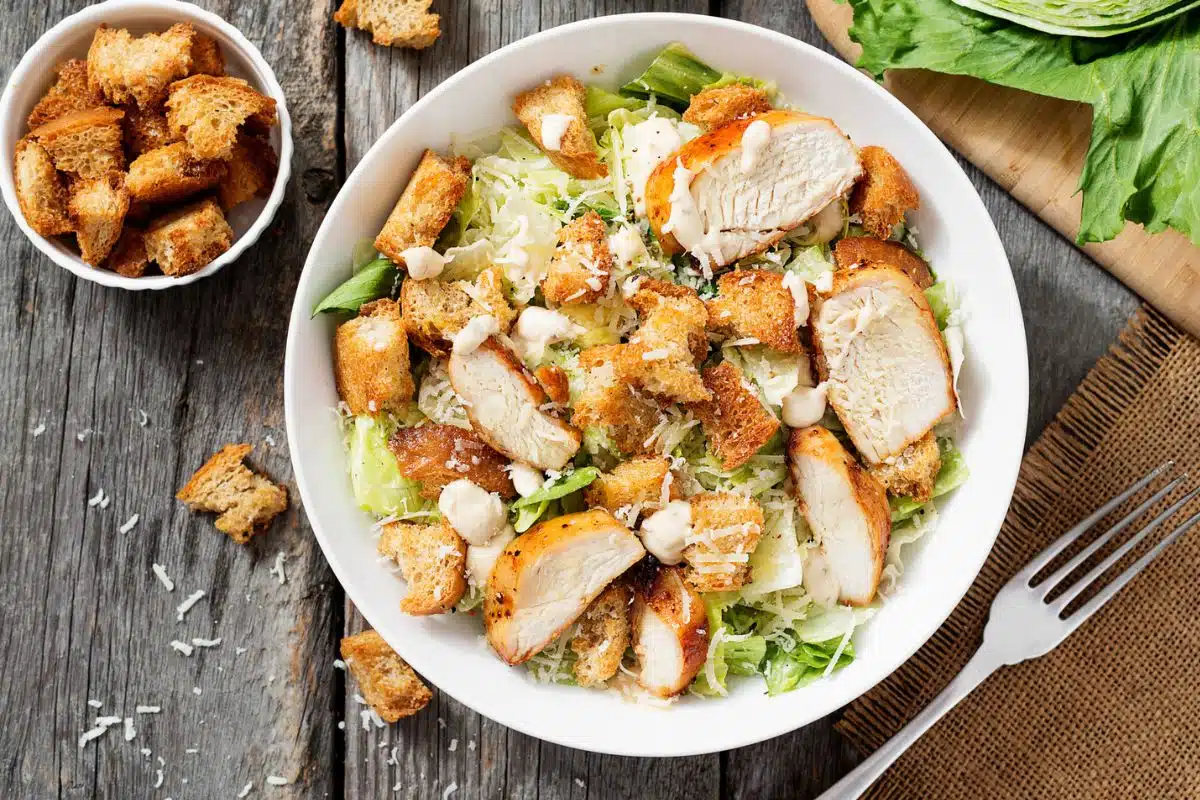 Caesar salad in a white bowl on a wood table.