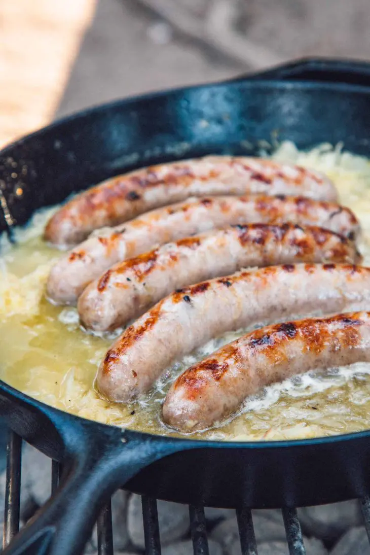 Beer brats simmering in beer and sauerkraut in a cast iron skillet