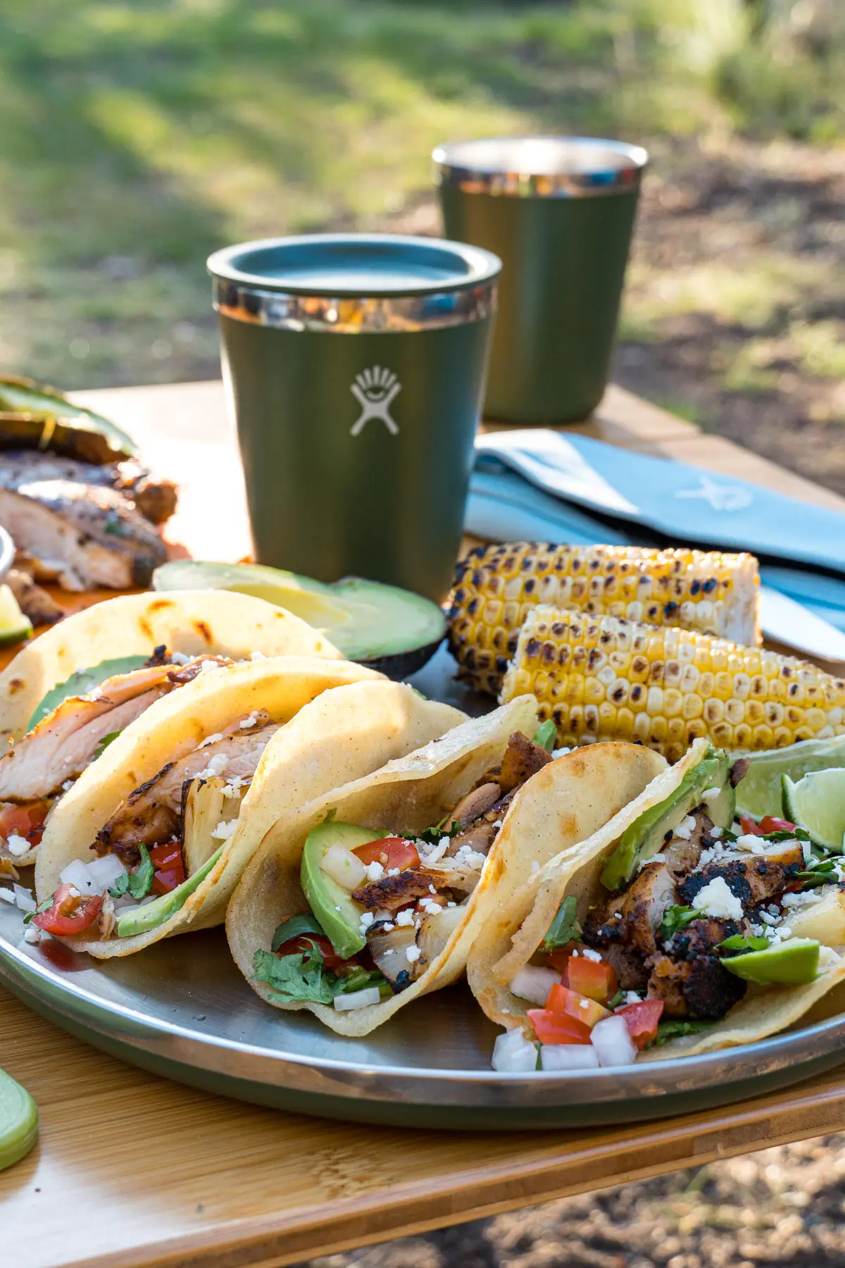 Four grilled chicken tacos on a plate with a green drinking glass in the background