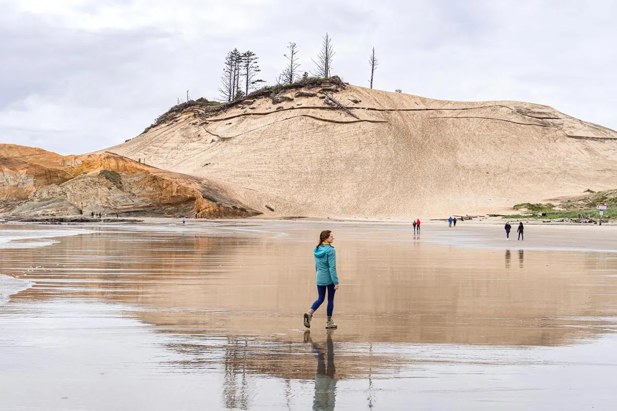 Megan walking on a beach towards a large sand dune.