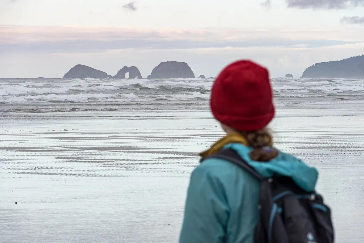 Megan stands on a beach and looks out at rock formations.