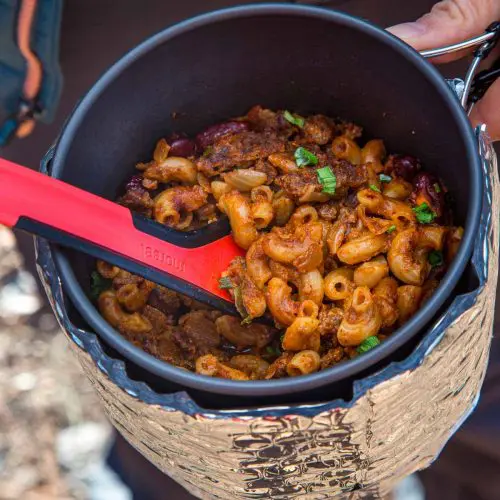 Megan holding a pot and using a spoon to scoop up chili mac.