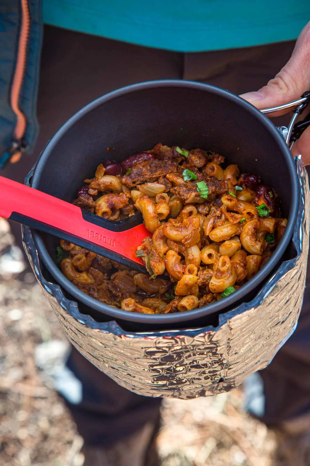 Megan holding a pot and using a spoon to scoop up chili mac.