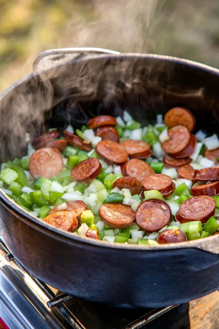 Steam rising from a Dutch oven full of vegetables and sausage