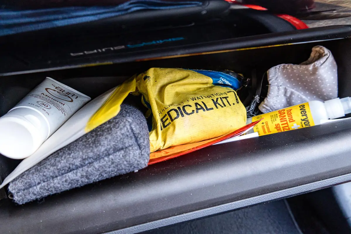 An open glove box with a first aid kit, hand sanitizer, sunscreen, and an organizing pouch