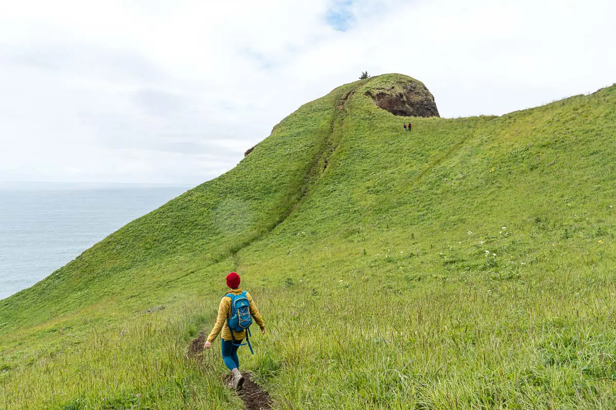 Megan walks on a trail leading up to a grassy knoll.