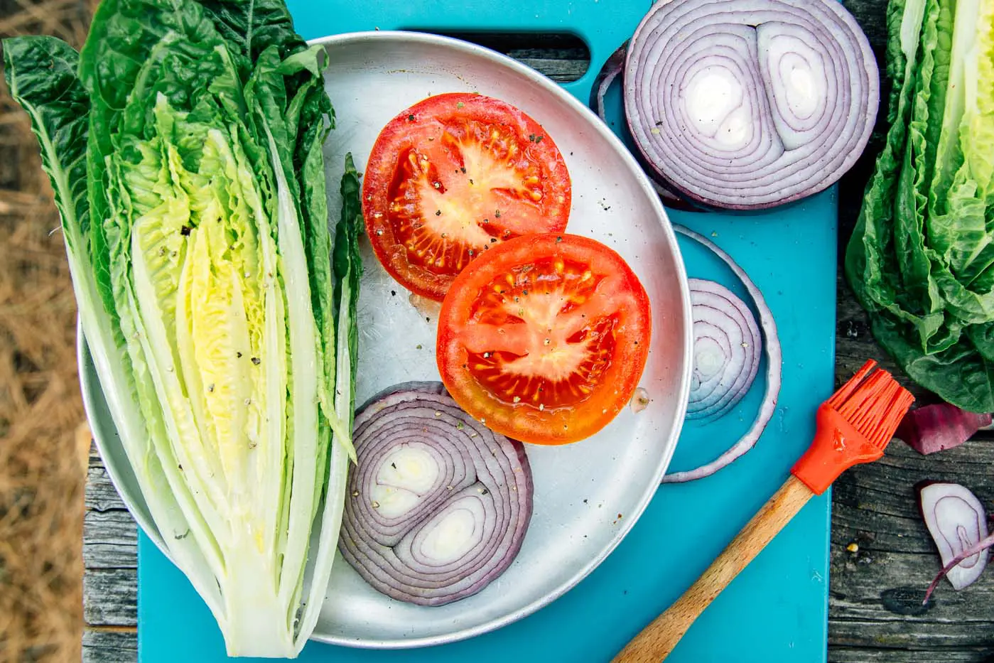 Ingredients for grilled burgers including tomatoes, red onions, and romaine lettuce