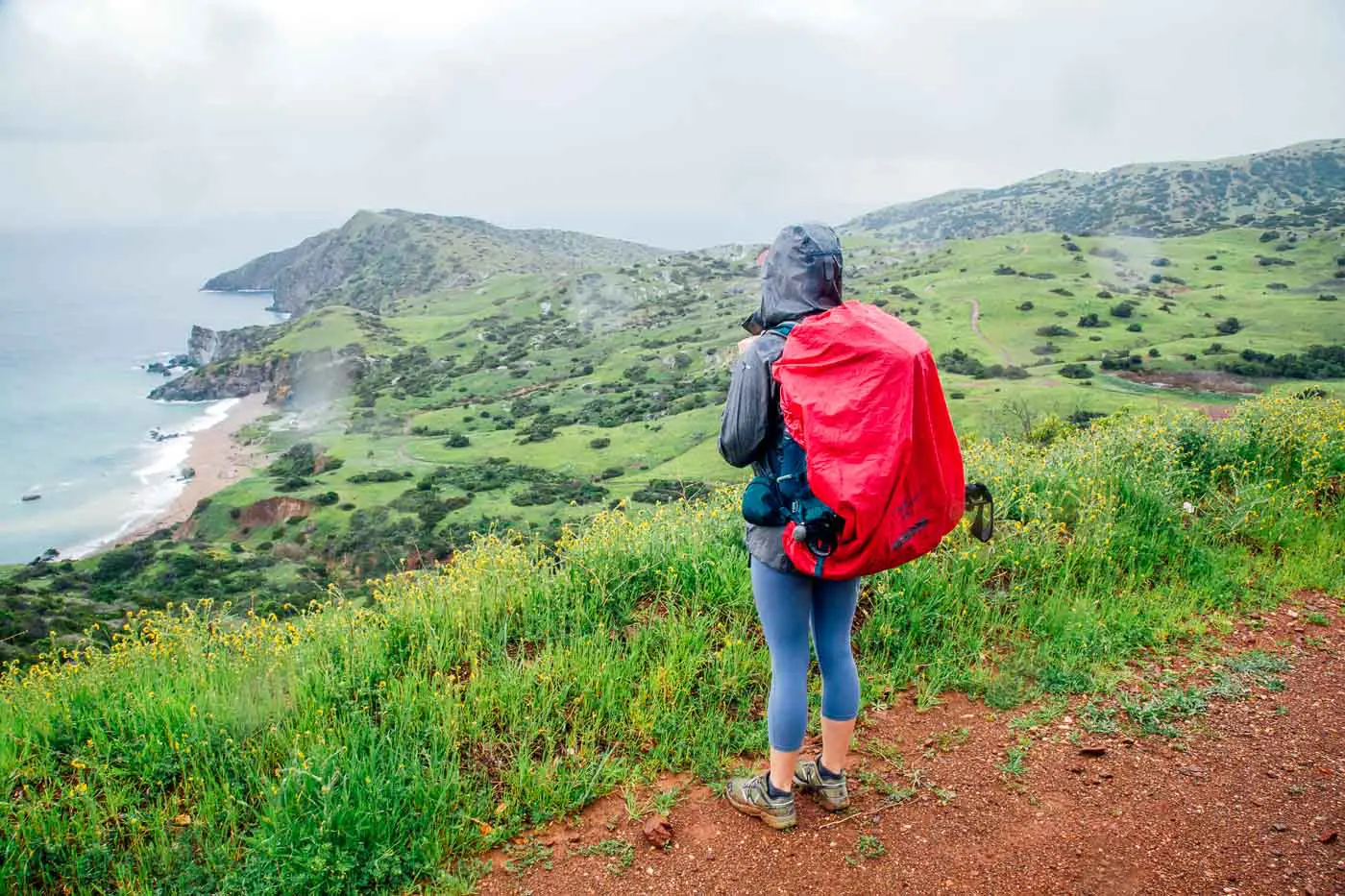 Woman on a trail overlook, looking out on the island and the ocean. The skies are rainy and she is wearing a rain jacket.