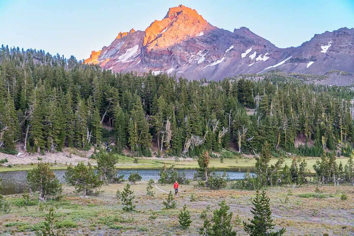 Michael hiking through a meadow with a mountain peak in the background